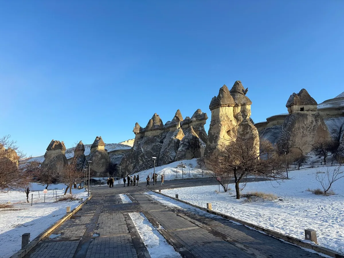 Eine Straße mit Schnee am Rand führt an hellen Feenkaminen und kahlen Bäumen unter klarem blauem Himmel vorbei