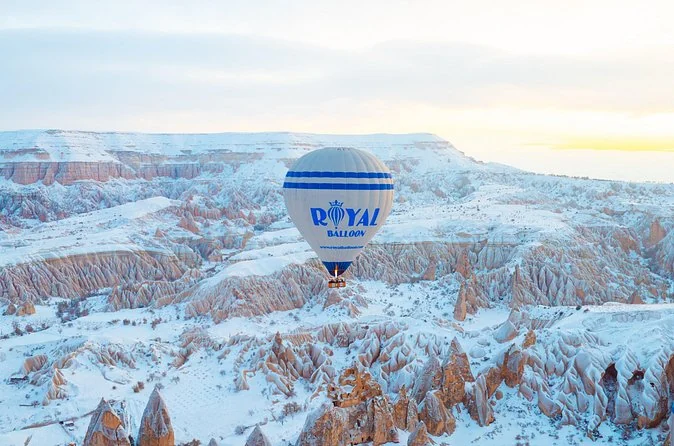 Una mongolfiera Royal blu e bianca che fluttua sopra valli innevate di formazioni rocciose