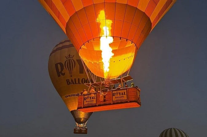 La fiamma di un bruciatore che illumina l'interno di una mongolfiera gialla sopra il suo cesto