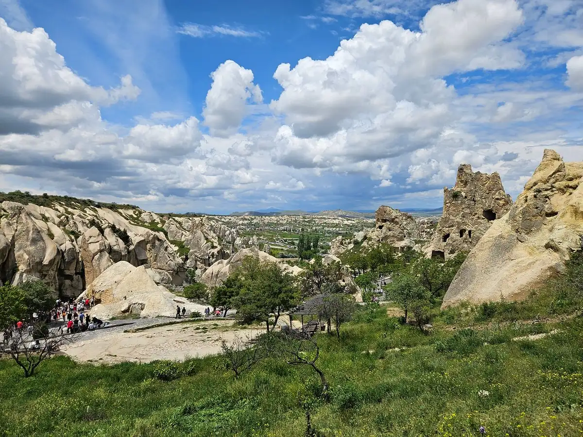 A green valley floor with trees and pale fairy chimneys under a big sky with white clouds